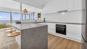 A modern kitchen with a large island, white cabinetry, and a view to the outside. - Pambula Little Beach House (Pambula Beach)