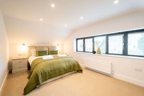 A bedroom with a bed, bedside tables, a radiator, and a window with a view.