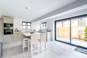 A modern kitchen with a large island, built-in appliances, and a sliding glass door to the backyard. - The Lodge, Private Parking & Garden (Gloucestershire)