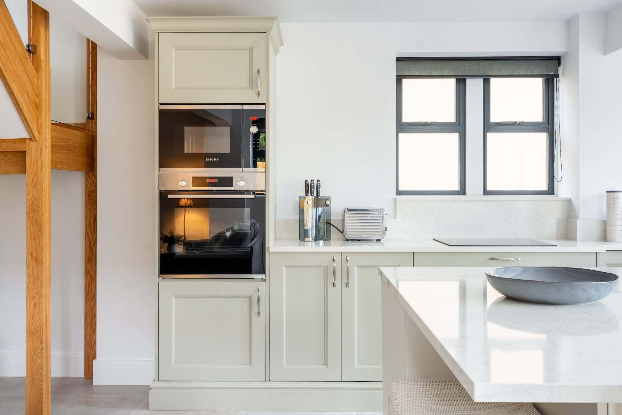 A modern kitchen with white cabinetry, a Bosch oven, a toaster, and a window above the sink.