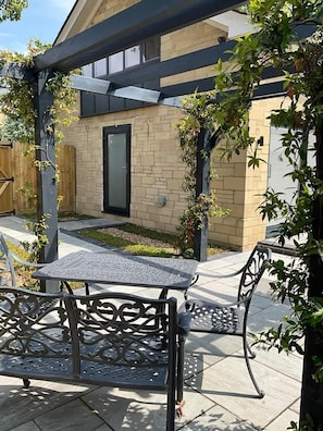 An outdoor patio area with a metal table and chairs, a brick building in the background, and a wooden fence.