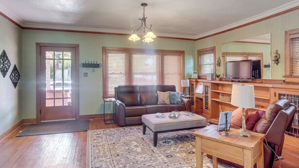 A living room with a brown leather sofa, a wooden coffee table, a rug, and a television on a wooden stand. - Walk to Main Street: Charming Roswell Home! (Roswell)