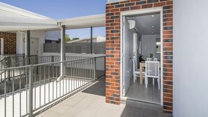 A modern building with a covered outdoor area, a staircase, and a door leading to an interior space with a table and chairs. - Sunny 2-Bed in Quiet Location with Balcony (Cannington)
