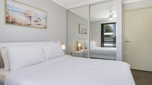 A bedroom with a large bed, a nightstand with a lamp, a ceiling fan, and a sliding glass door leading to a balcony. - Sunny 2-Bed in Quiet Location with Balcony (Cannington)