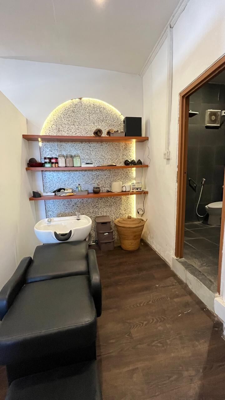 Een kleine badkamer met een wastafel, spiegel, planken met toiletartikelen, een massagetafel en een douchehoek.