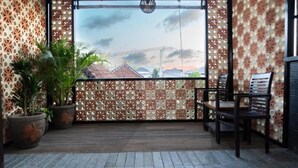 A balcony with a patterned fence, potted plants, and a view of buildings in the distance. - Eco Boo Boo - Green Genesis (Jimbaran)