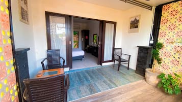 Quarto de hotel com uma cama, escrivaninha, duas cadeiras, planta em vaso e vista para o exterior.