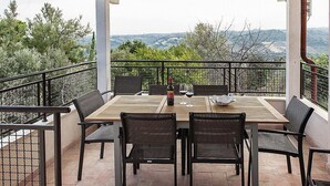 A covered outdoor dining area with a table and chairs, overlooking a scenic landscape.