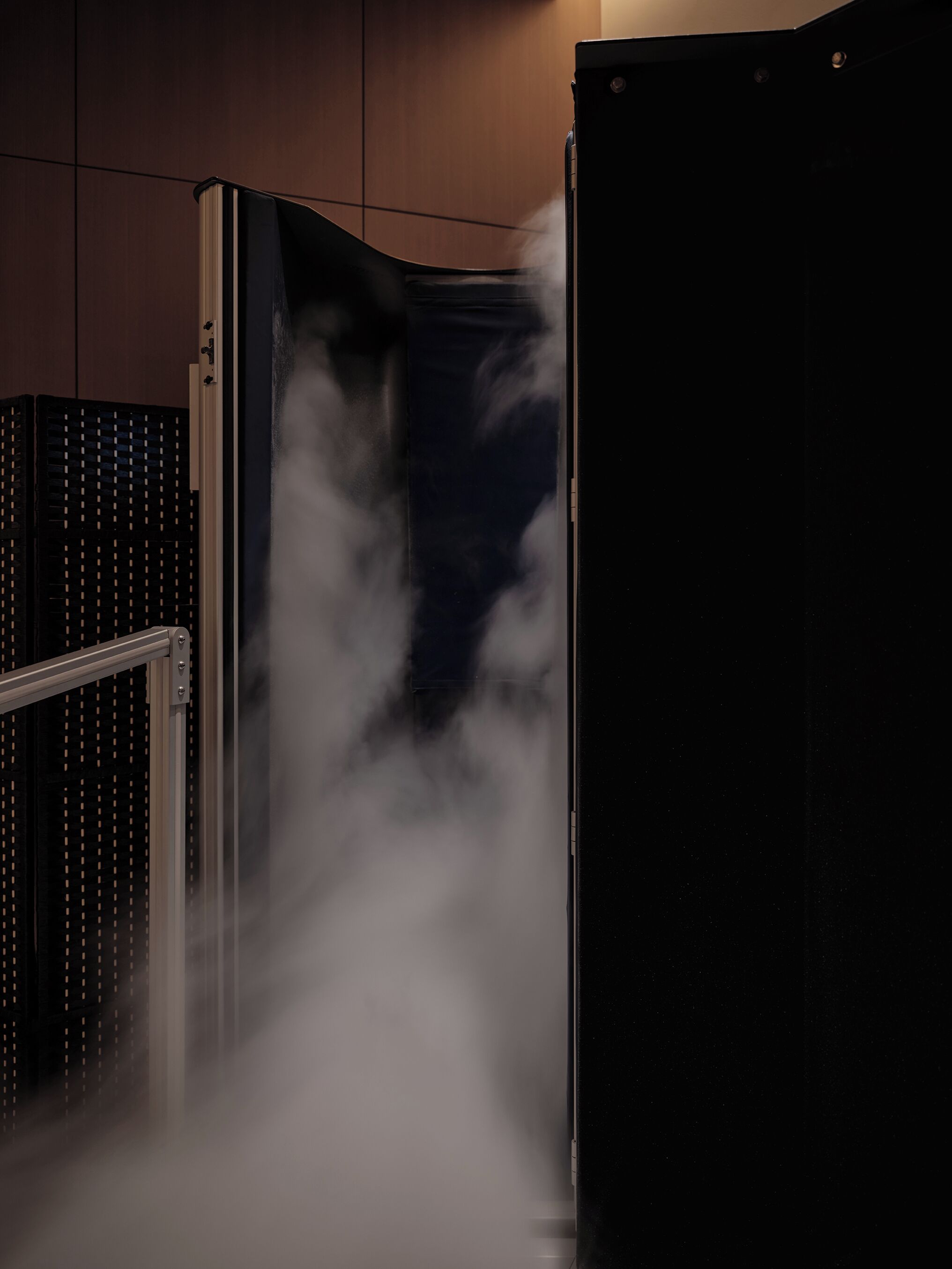 A room with a large, dark-colored cabinet and a metallic structure, possibly a radiator or vent, emitting steam or mist.