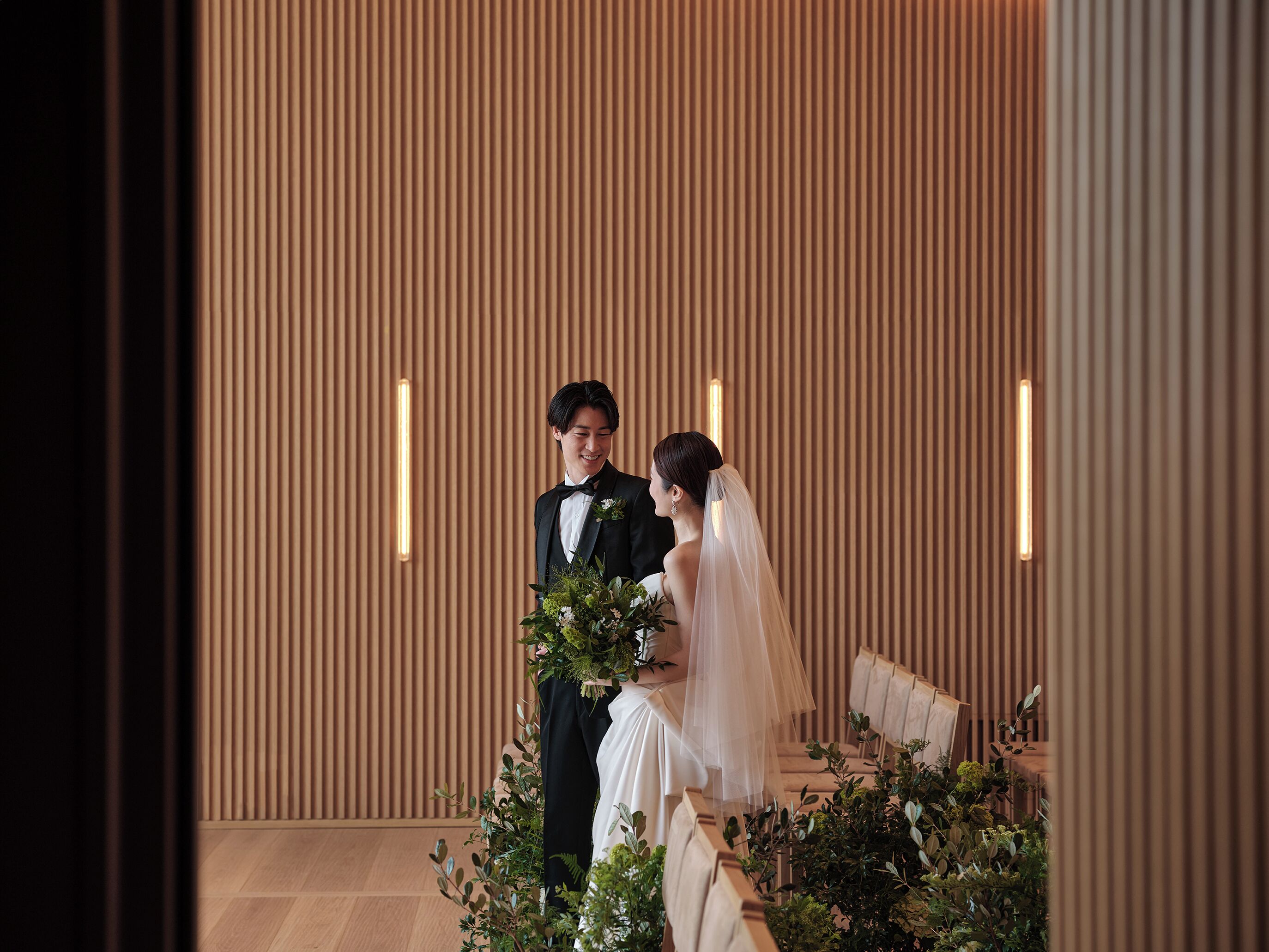 A couple seated on a bench in a room with vertical wooden slats on the walls and a light fixture above.