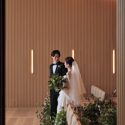 A couple seated on a bench in a room with vertical wooden slats on the walls and a light fixture above.