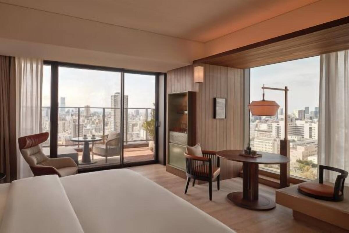A hotel room with a large bed, a balcony with a table and chairs, and a city view.