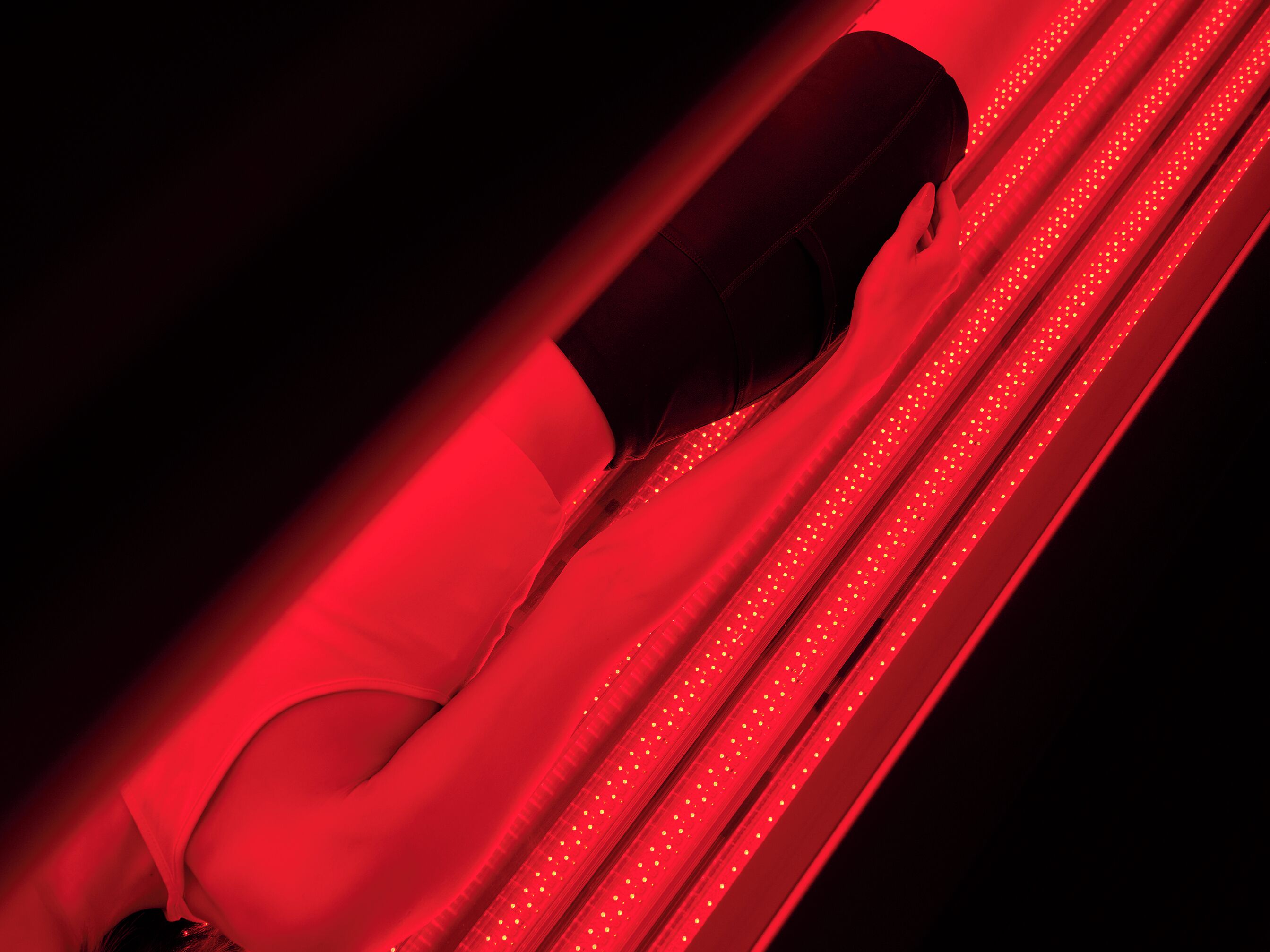 A person lying on a red-lit surface with a curved structure.