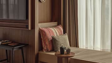 Una habitación acogedora con pared de paneles de madera, un televisor de pantalla plana grande, una zona de estar cómoda con cojines, una pequeña mesa redonda con una tetera y una ventana con cortinas.