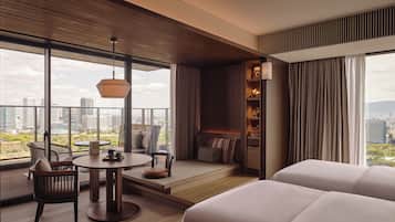 A modern hotel room with a large balcony, a dining area, and a cozy seating space with a view of the cityscape.
