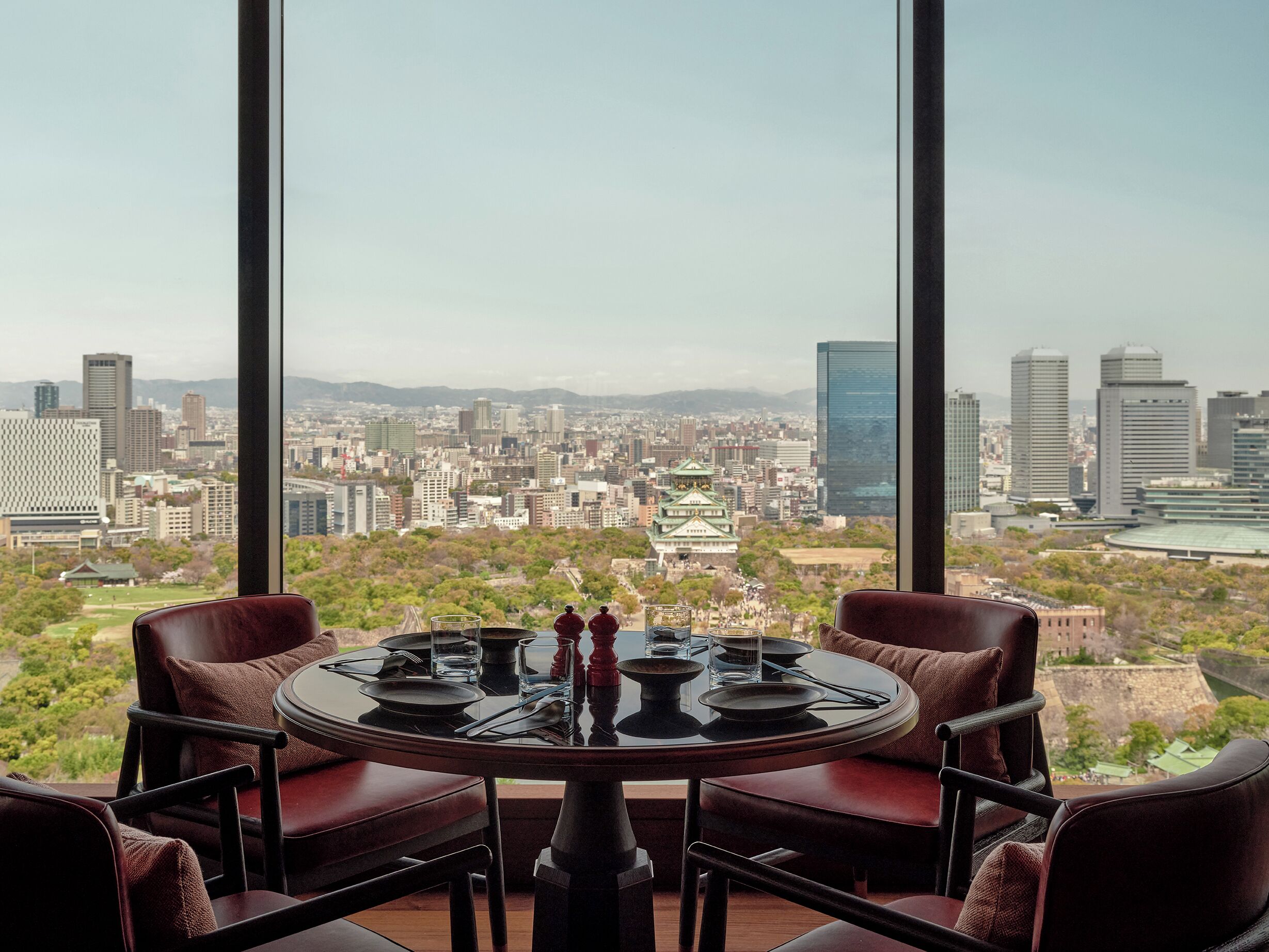 Comedor con una mesa dispuesta para cuatro, con vistas a un paisaje urbano que incluye edificios modernos y un castillo tradicional.