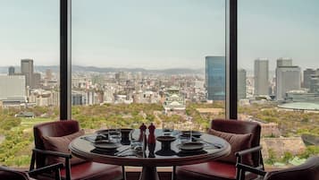 Comedor con una mesa dispuesta para cuatro, con vistas a un paisaje urbano que incluye edificios modernos y un castillo tradicional.