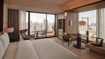 A hotel room with a large bed, a seating area with a table, and a city view through large windows.