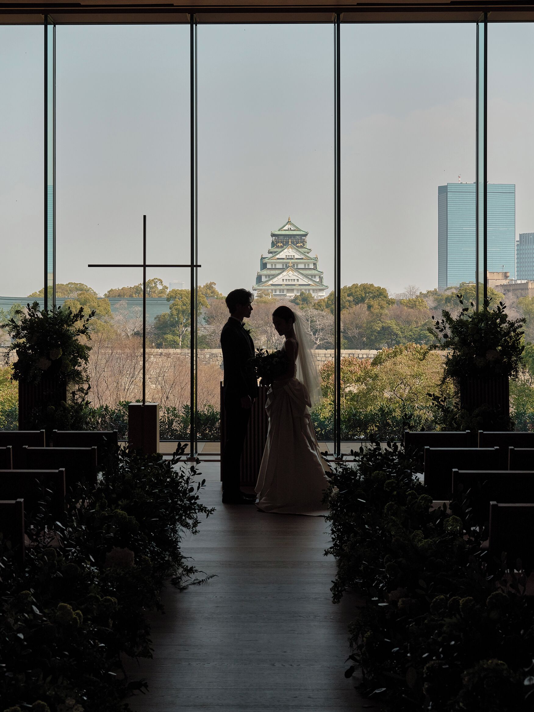 A couple standing in a ceremony aisle with a view of a traditional building and a modern skyscraper in the background.