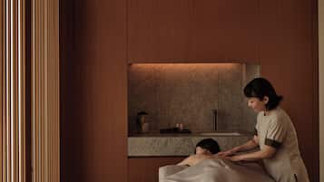 A spa room with wooden paneling, a massage table, and a person receiving a massage.