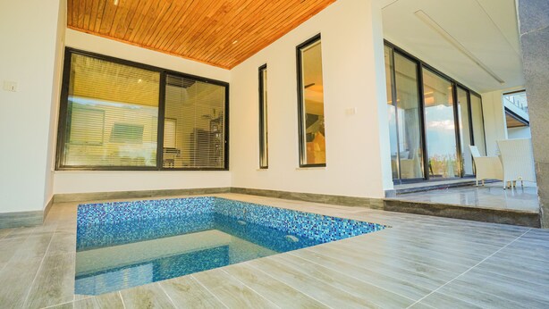 A modern indoor swimming pool with a wooden ceiling, large windows, and a tiled floor.