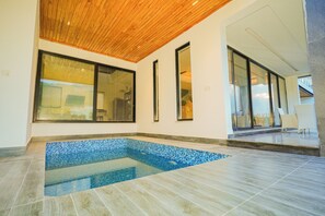 A modern indoor swimming pool with a wooden ceiling, large windows, and a tiled floor.
