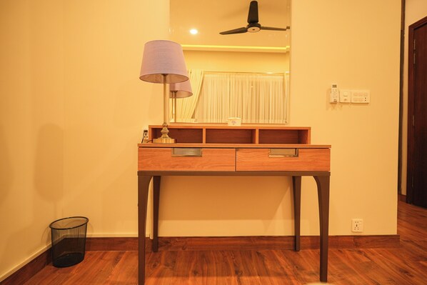 A wooden desk with drawers, a lamp, and a ceiling fan in a room with wooden flooring and a light-colored wall.