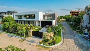 A modern two-story house with a garage, surrounded by greenery and a cobblestone street.