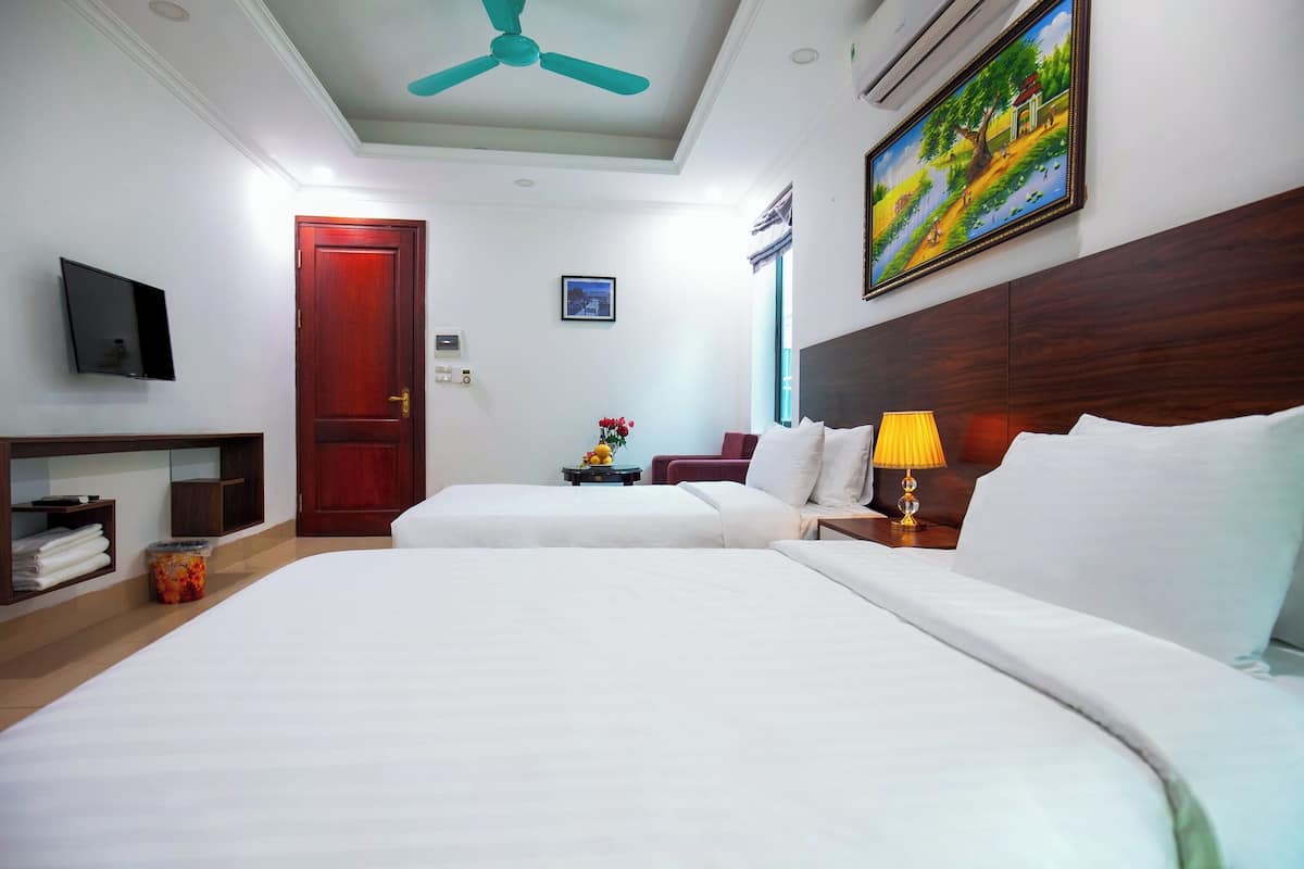 A hotel room with two beds, a ceiling fan, a TV, a painting, and a wooden headboard.