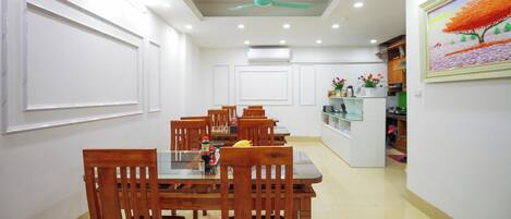 A dining area with wooden chairs and a glass table, white walls, and recessed ceiling lights.