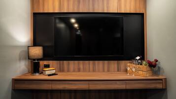 Un meuble de divertissement moderne comprenant un téléviseur à écran plat, une lampe, une télécommande et une boîte en bois contenant une bouteille de vin et des fleurs.