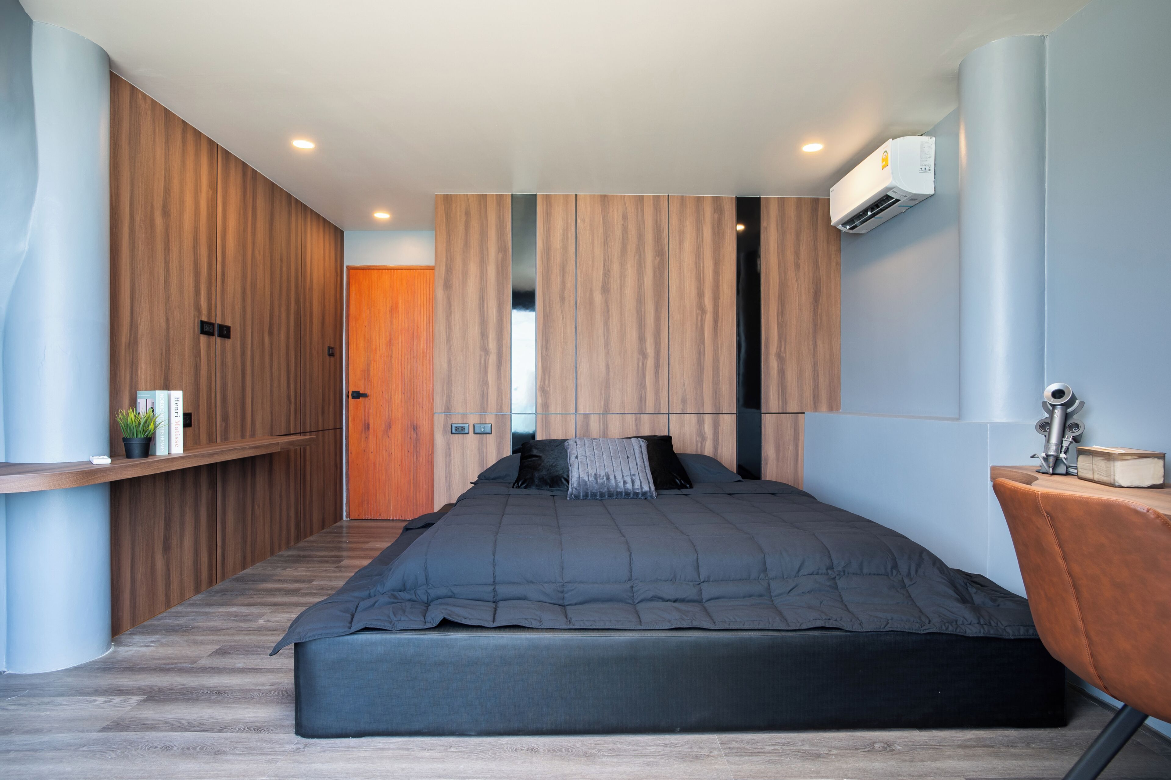 Un dormitorio moderno con una cama grande, paredes de paneles de madera, un escritorio pequeño y un equipo de aire acondicionado.