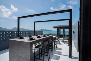 Un área de comedor exterior moderna con barra, sillas y vista al mar.