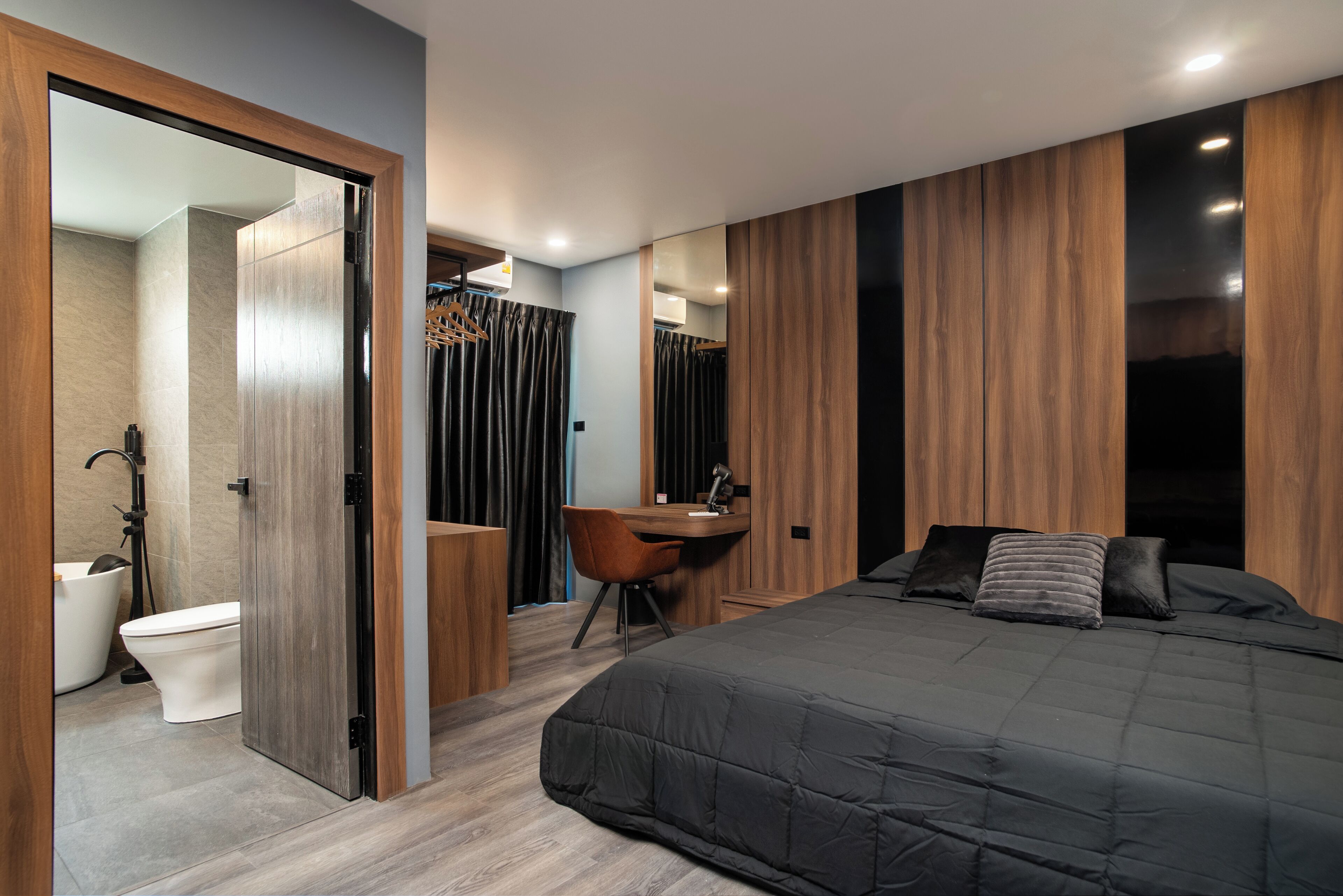A modern bedroom with a large bed, a desk, and a bathroom.