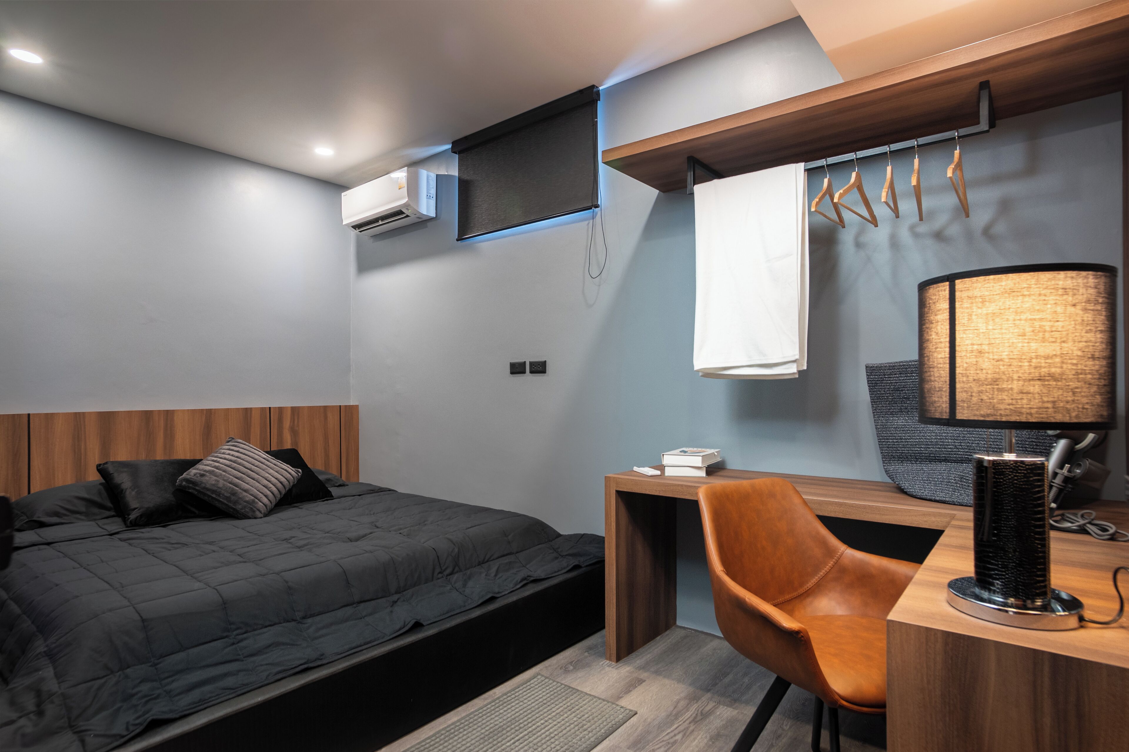 A modern hotel room with a bed, a desk, a chair, a lamp, and a hanging clothes rack.