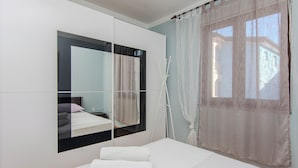 A modern bedroom with a large mirror, a bed, and a window with sheer curtains. - Holiday home Suric (Privlaka)