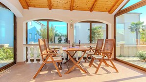 A covered patio with wooden furniture and large windows. - Holiday home Suric (Privlaka)