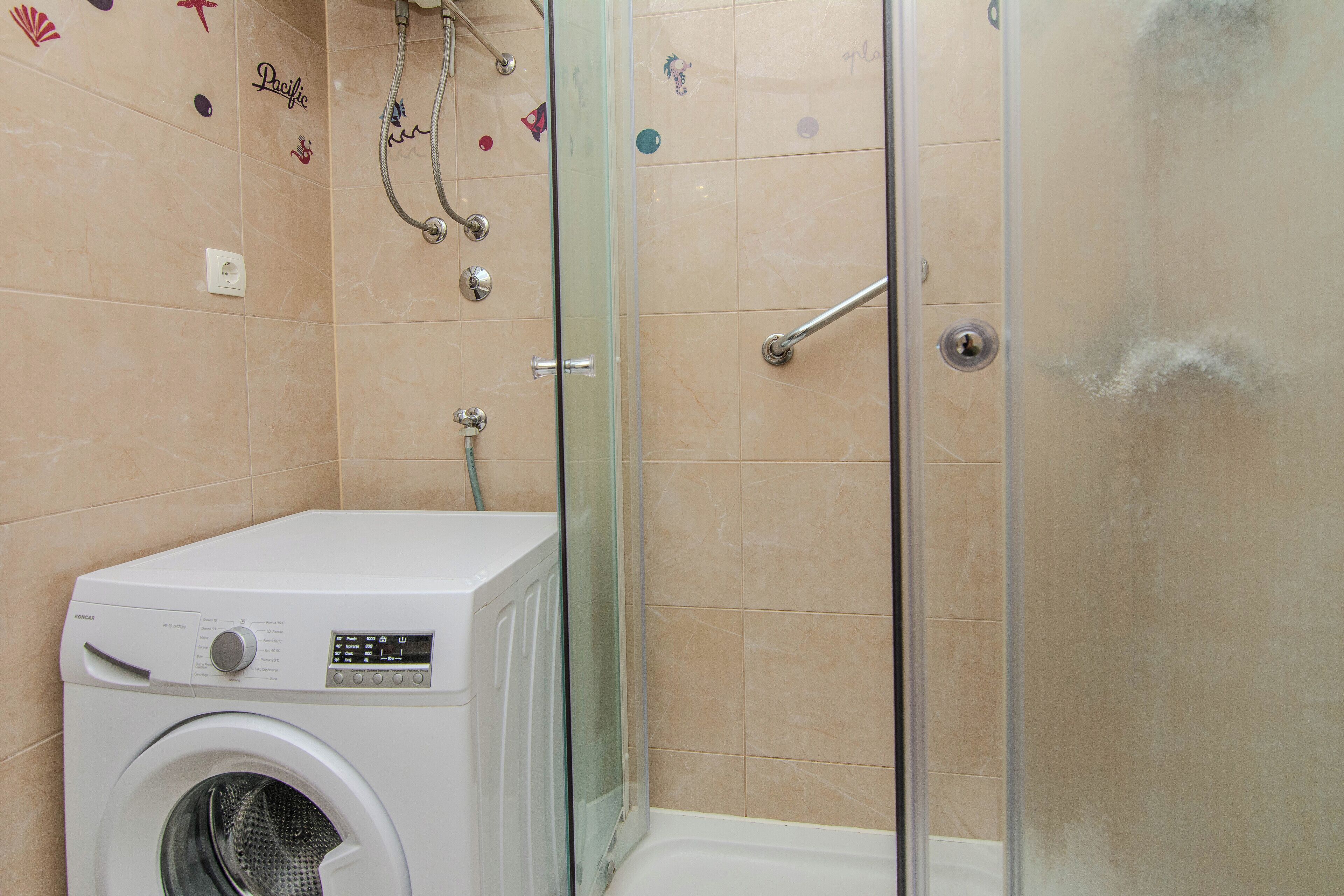 A compact bathroom with a washing machine, a glass shower enclosure, and tiled walls.