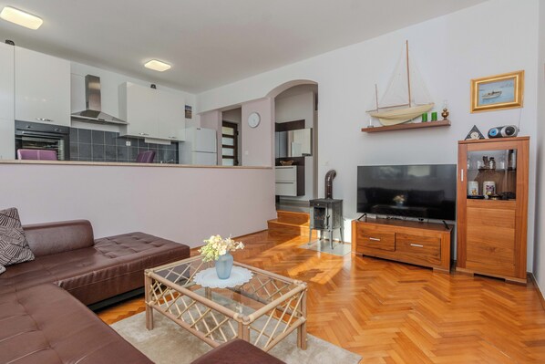 A modern living room with a brown leather sofa, a glass coffee table with a vase, a flat-screen TV, and a wooden cabinet.