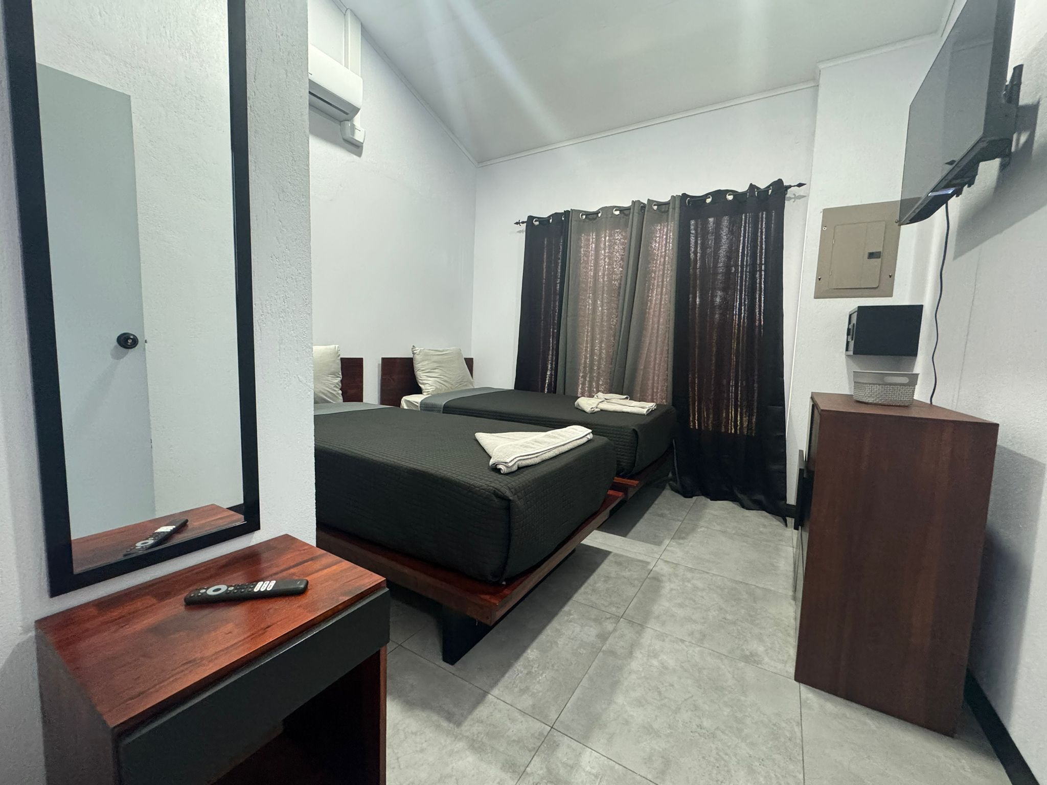 Une chambre d’hôtel avec deux lits, un bureau en bois, un miroir, une télévision et une armoire.