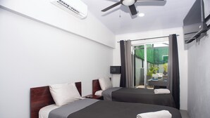 A hotel room with two beds, a ceiling fan, an air conditioning unit, and a view of the outdoors through a glass door. - Party Villa with Pool, Walk to Clubs (Jacó)