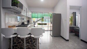 A modern kitchen with white cabinets, a stone countertop, and a dining area with white chairs. - Party Villa with Pool, Walk to Clubs (Jacó)