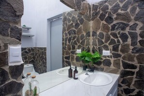 Une salle de bain avec un mur en pierre, un lavabo blanc et un miroir.