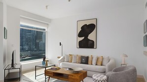 Ein modernes Wohnzimmer mit großem Fenster, einer Couch, einem Couchtisch und einem gemusterten Hocker.