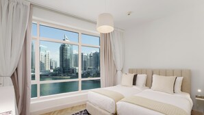 Ein Hotelzimmer mit großem Fenster und Blick auf die Stadt, zwei Betten, einem modernen Kopfteil und einem gemusterten Teppich.