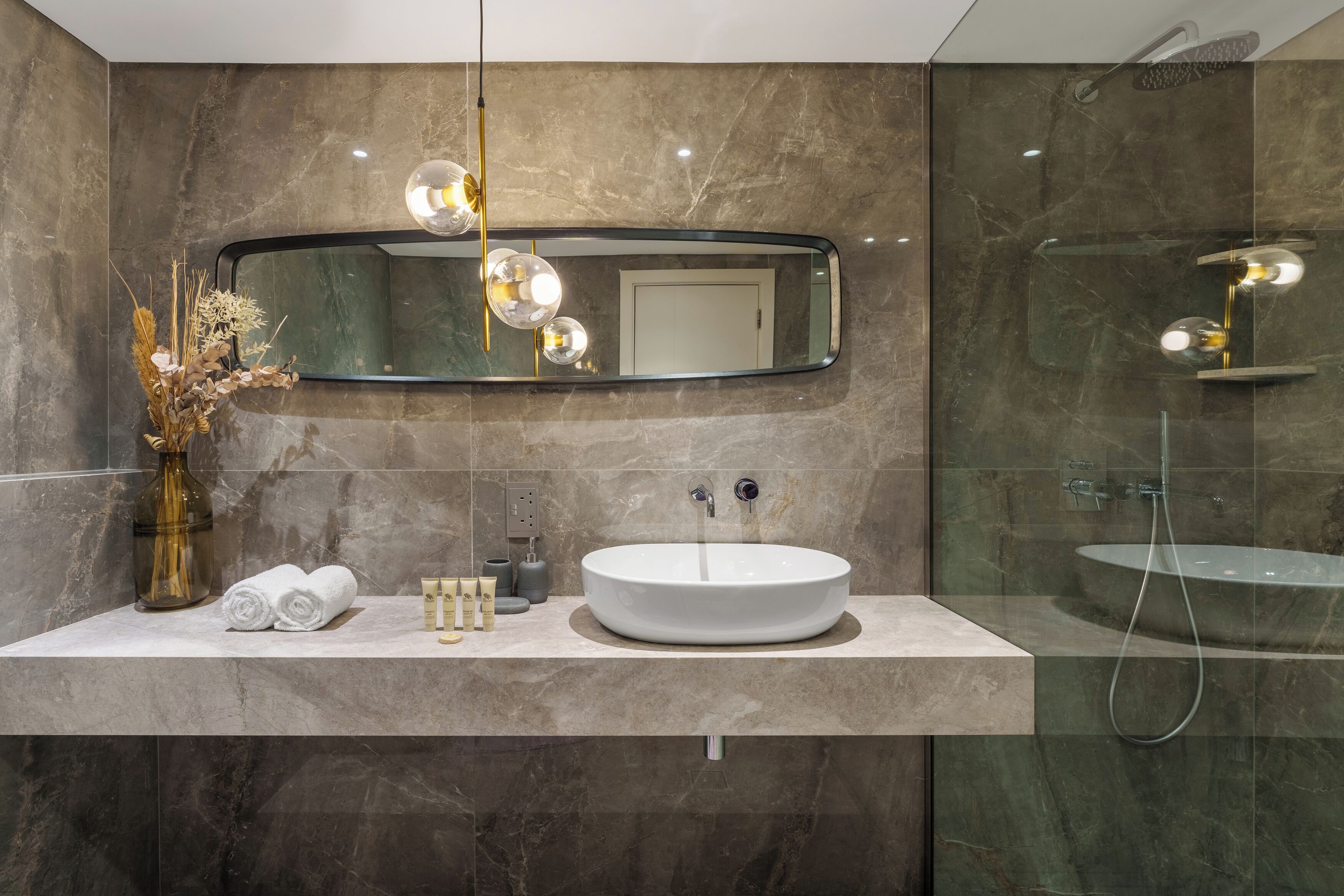 Un baño moderno con un lavabo redondo, un espejo grande y una ducha con cerramiento de vidrio.