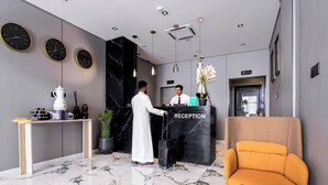 A reception area with a marble floor, a reception desk, a receptionist, a guest with luggage, and a sofa. - Arjan Park Al Narjis (Riyadh)