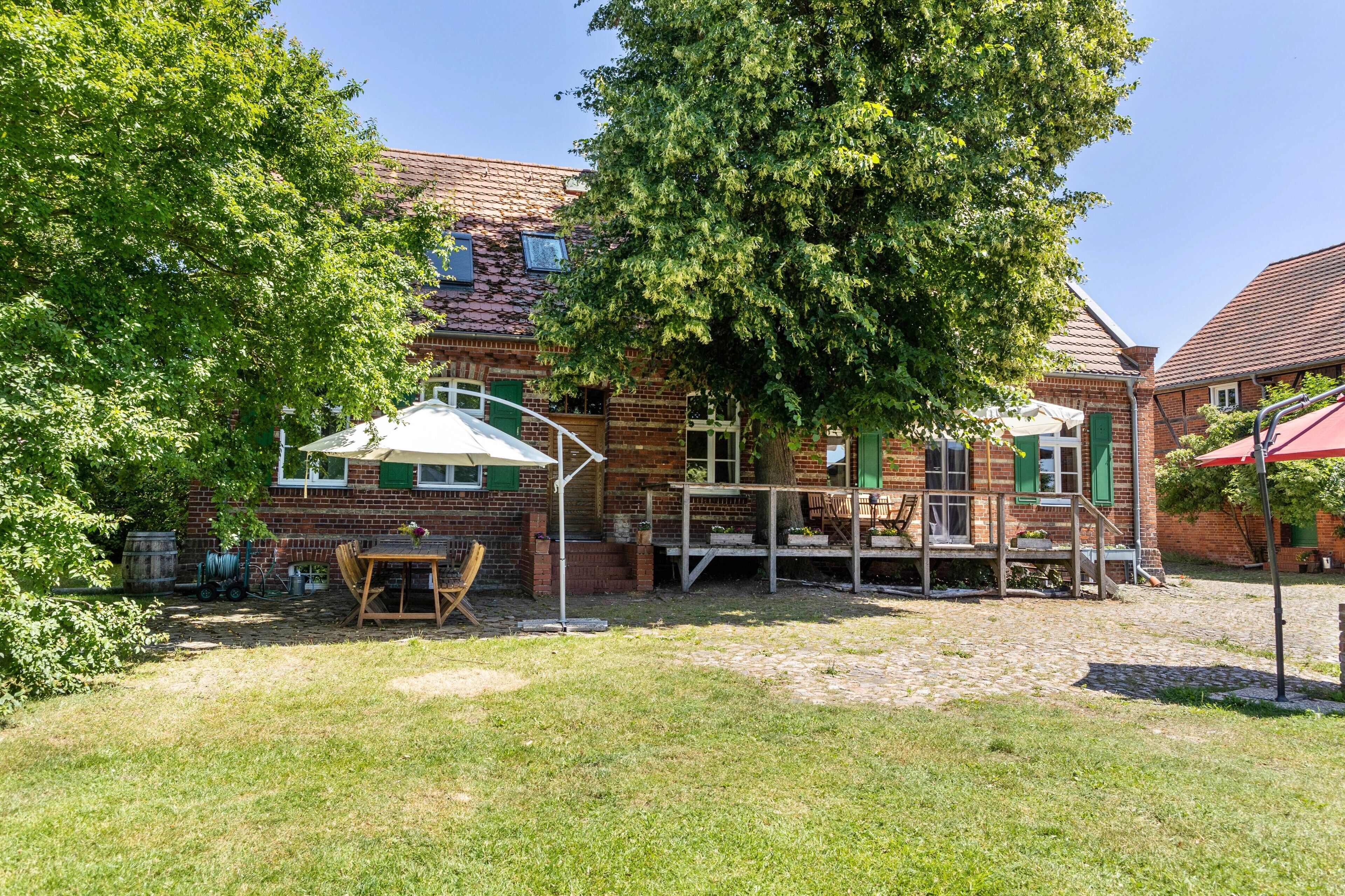 A brick building with a wooden deck, a table, and chairs in the yard.