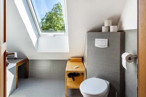 Une salle de bain moderne dotée d’un puits de lumière, d’un banc en bois, de toilettes et d’un porte-serviettes.