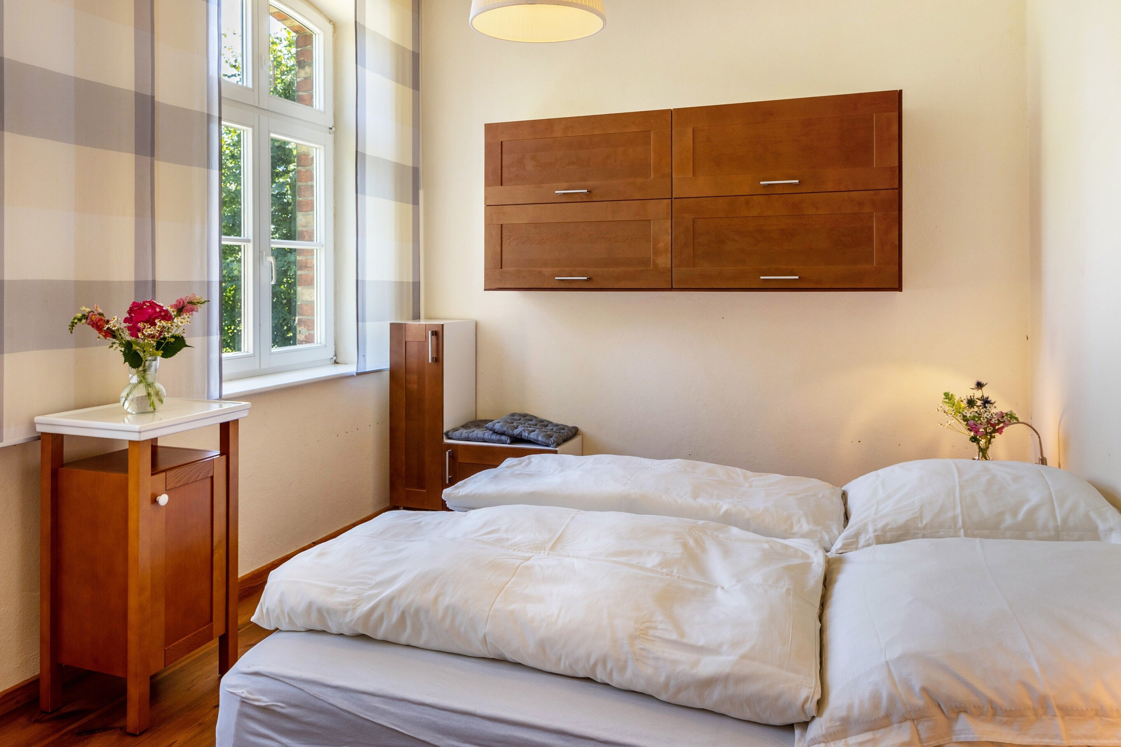 Une chambre à coucher comprenant un lit, une table de chevet, une commode, une fenêtre et un meuble fixé au mur.